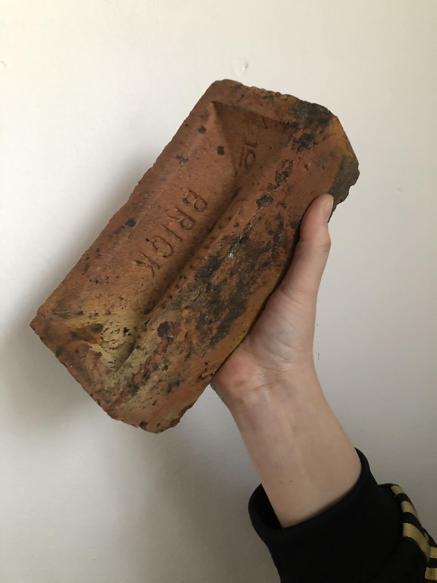 Made from this Land Emma Edmondson. A hand holding a London Brick brick in the air.